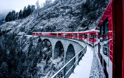 The Linia Alva homepage: a red train curving over a snow-covered stone viaduct through winter forest.