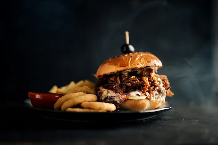 A burger with fries and onion rings on a metal tray.