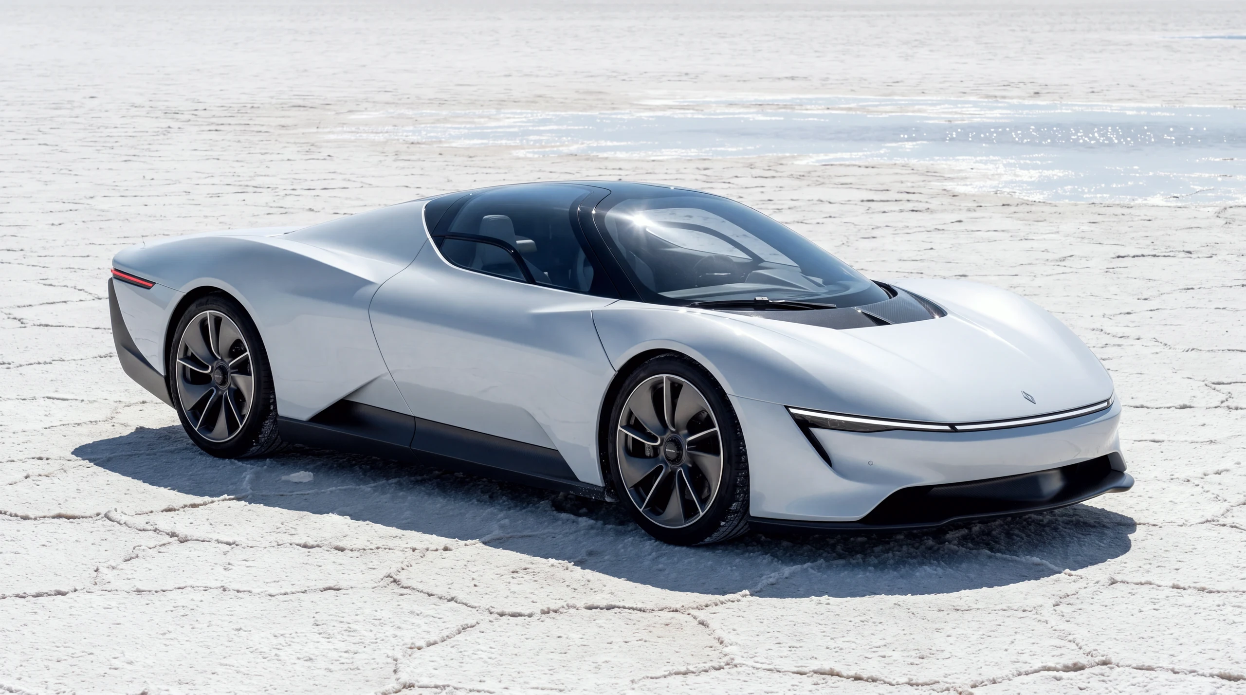 The T1 MONOLIT on the Weiss Flat: a low glacier-white single-seat record machine with a full-width nose light-blade, heat shimmer on the salt horizon.