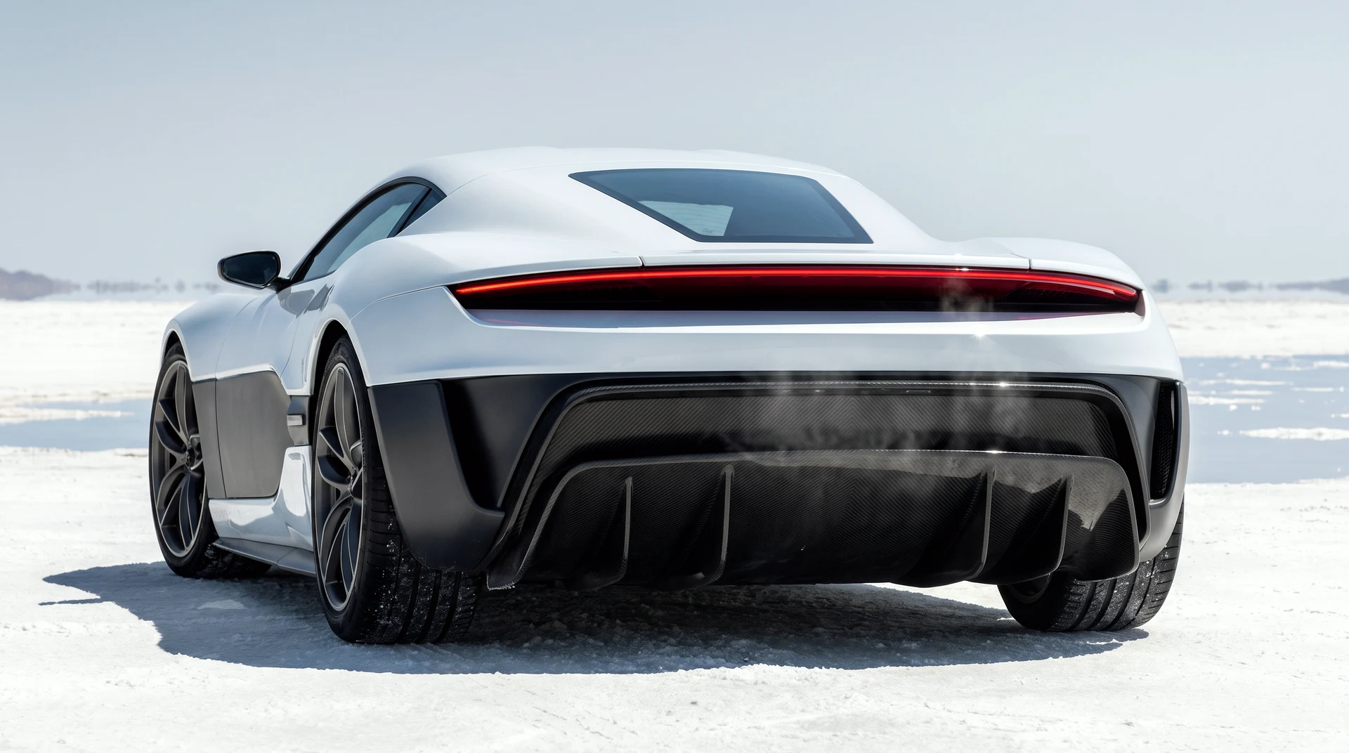 The MONOLIT from low behind: full-width tail light-blade glowing, carbon diffuser, heat haze rising off the salt.