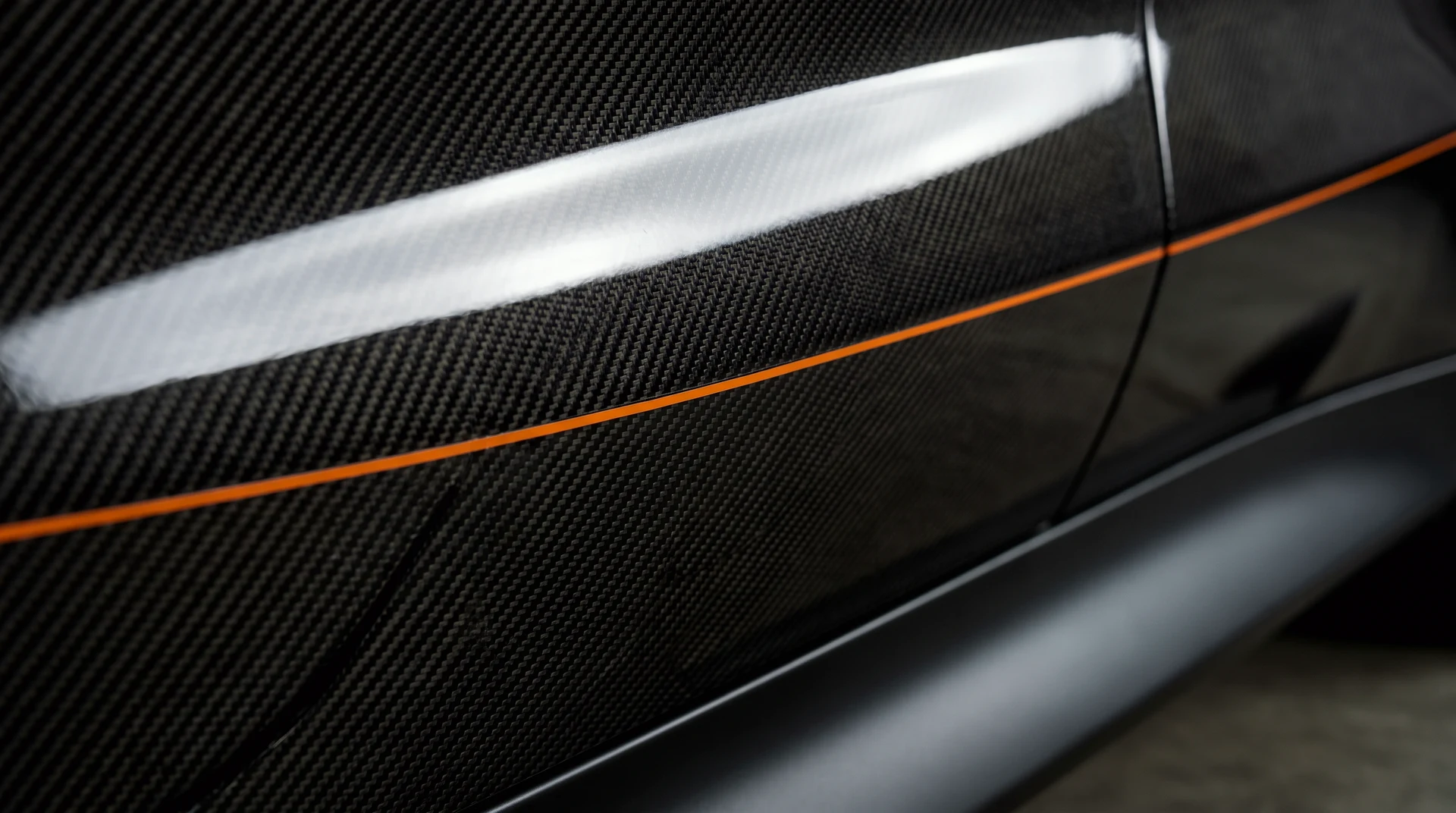 Macro of twill carbon fibre with a single thin signal-orange pinstripe.
