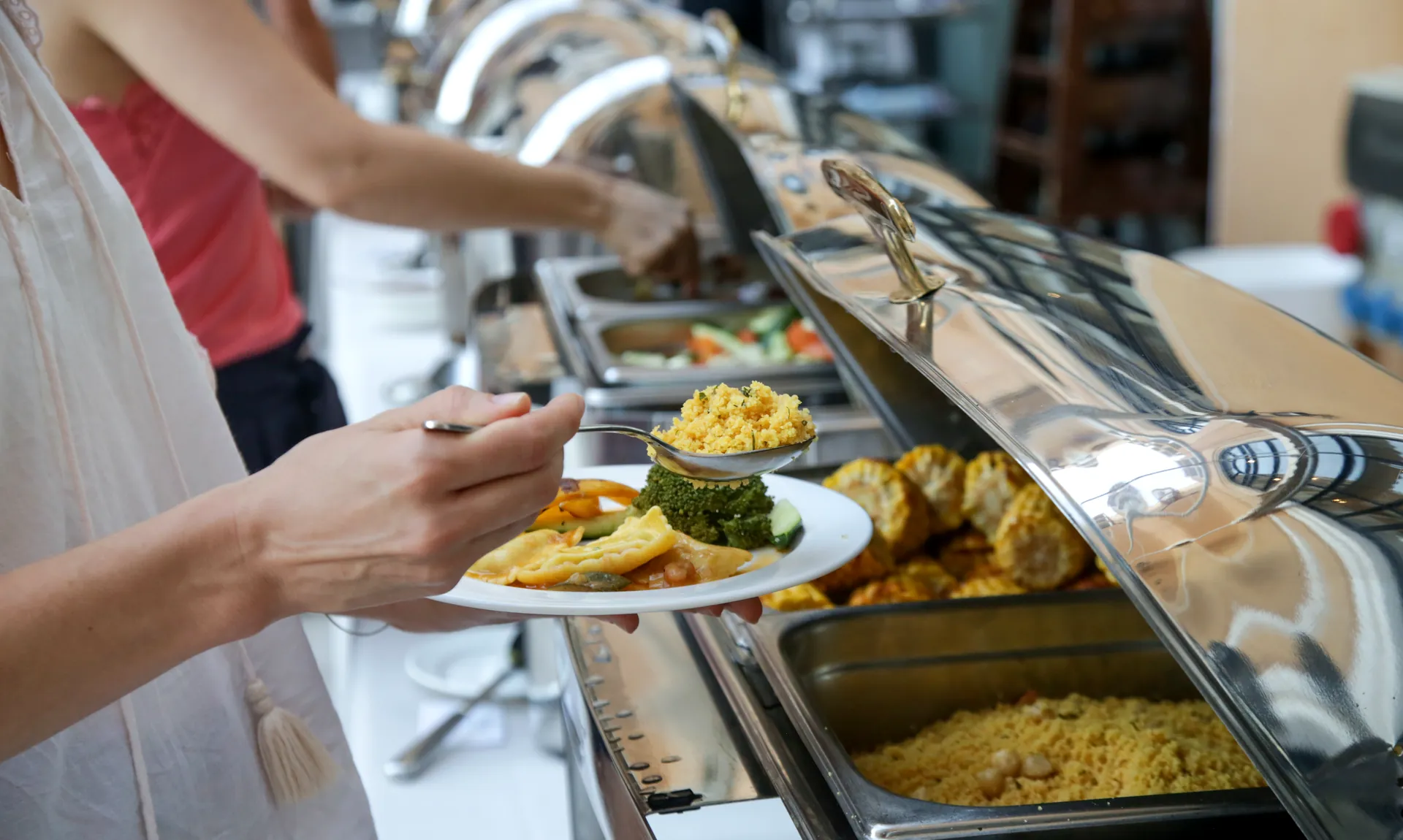 A guest fills a plate at the buffet line, trays of hot food stretching down the counter.