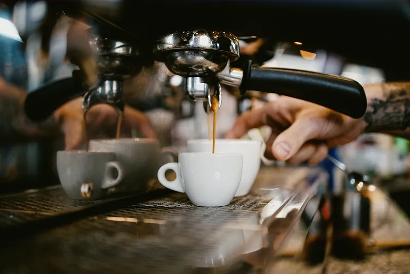 Espresso running from the group head into two small white cups on the machine's warm steel tray.