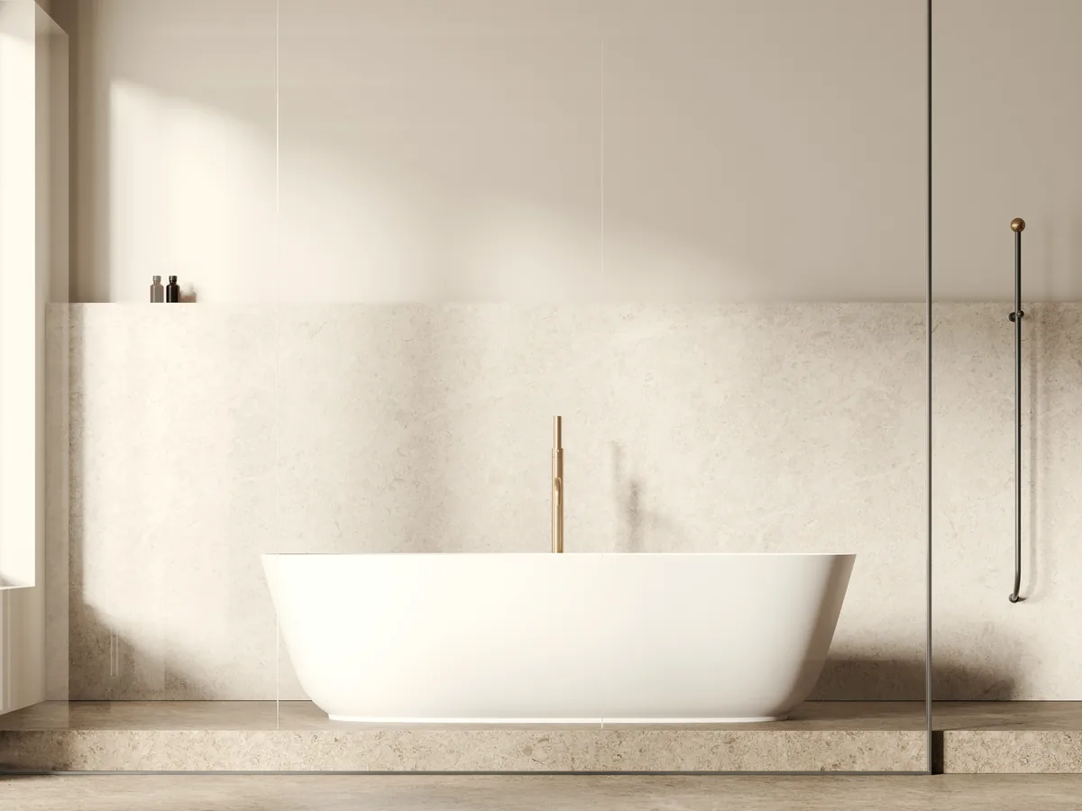 A deep white tub set against warm stone, brass taps, glass screen to one side.