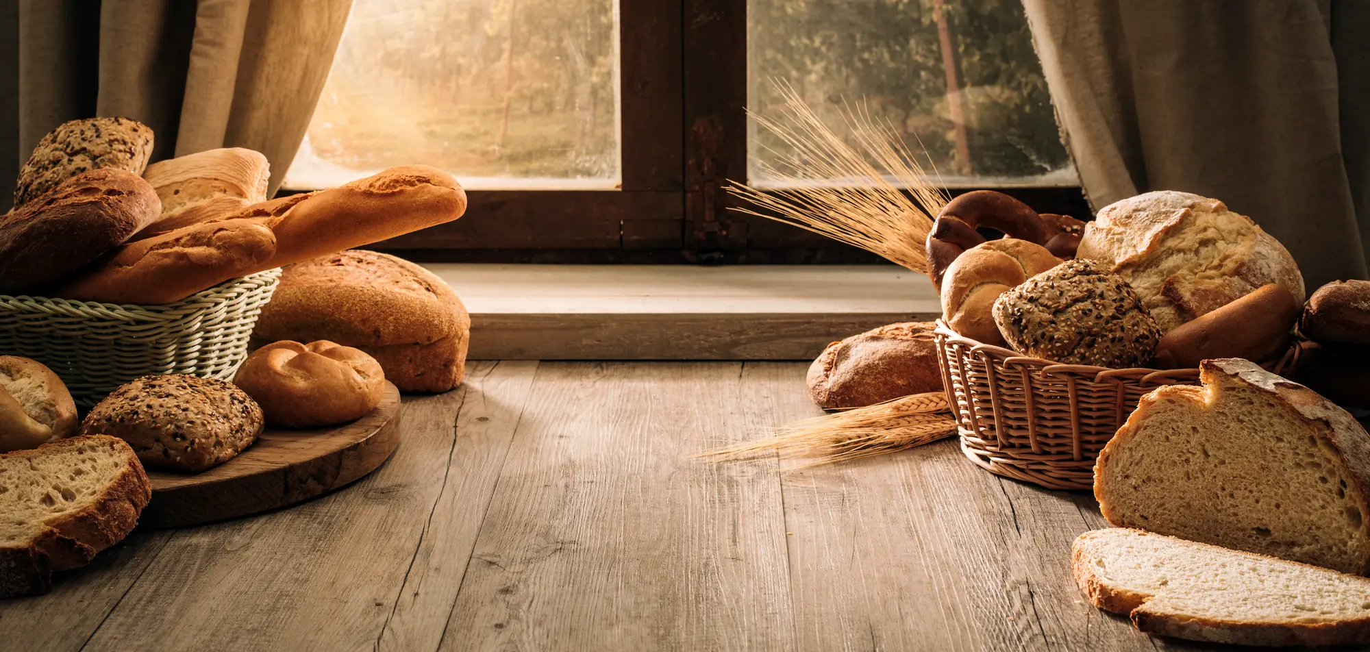 Loaves of bread stacked by a window at first light, wheat sheaves against the warm glass.
