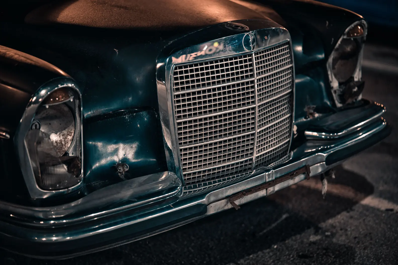 The chrome grille of a vintage saloon at night, lit warm from a streetlamp