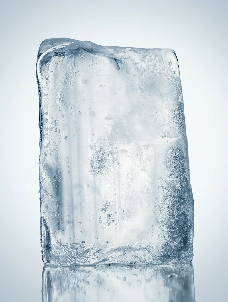 A single crystal-clear block of ice standing on a reflective steel surface.