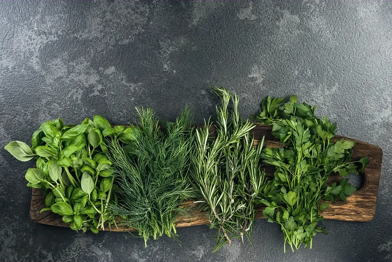 Bunches of basil, dill, rosemary and parsley laid on a weathered board against dark granite.