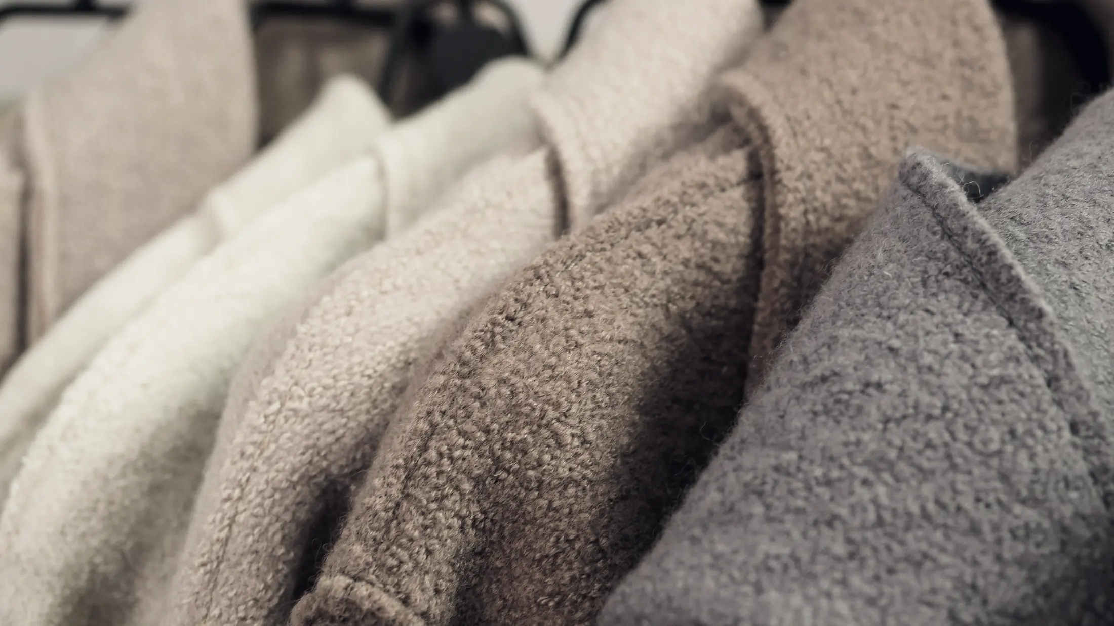 A rail of wool coats hanging in a quiet shop, photographed in low light.
