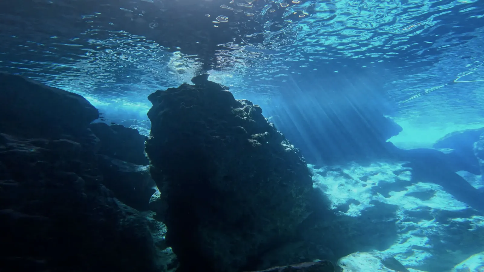 Sunbeams cutting through water above a rocky grotto