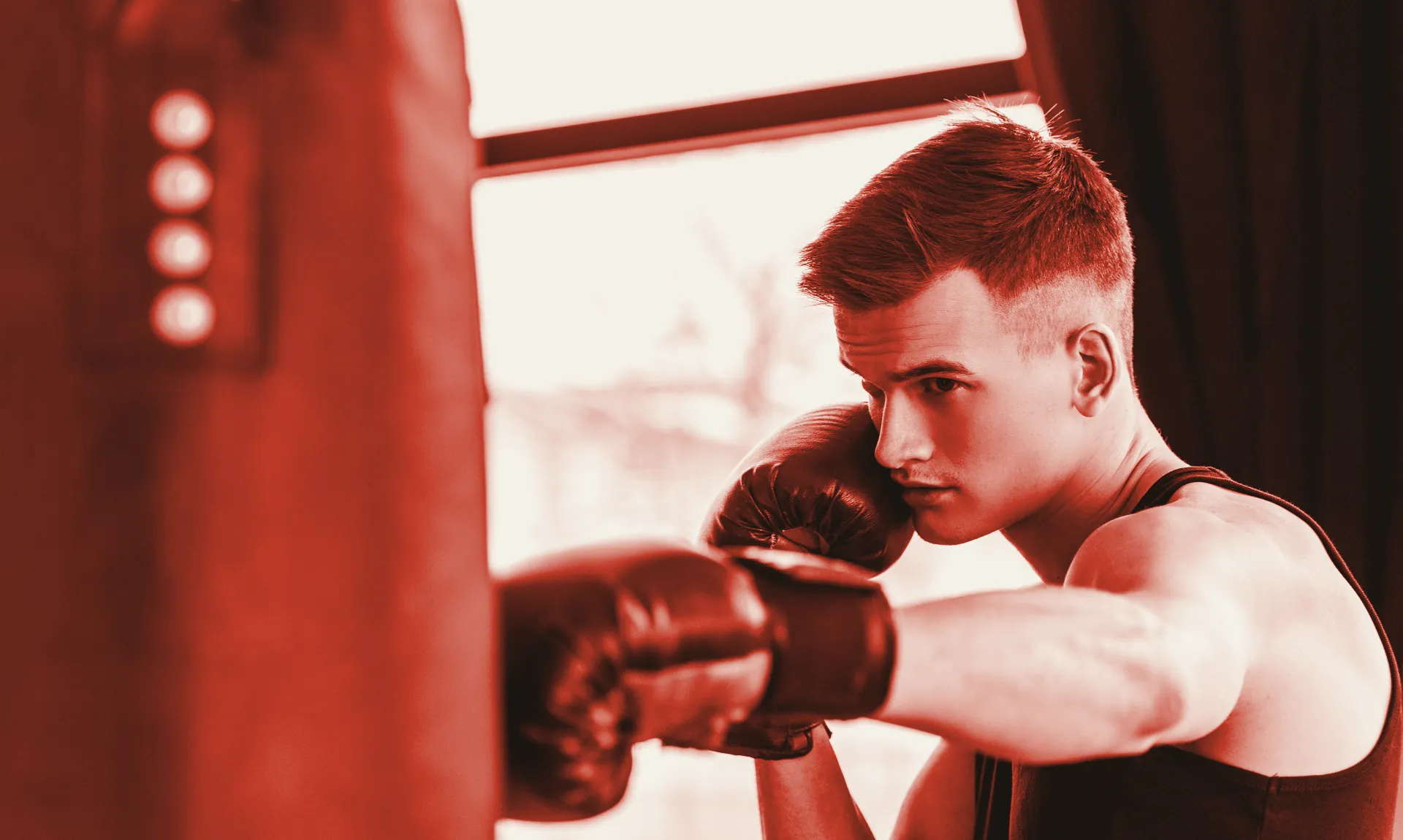 A boxer works a heavy bag by the window, printed in the gym's red duotone.