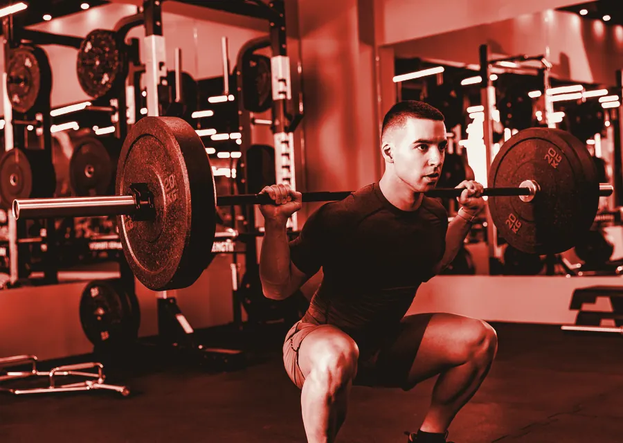 A lifter sets up under a loaded bar in the squat rack, printed in red duotone.