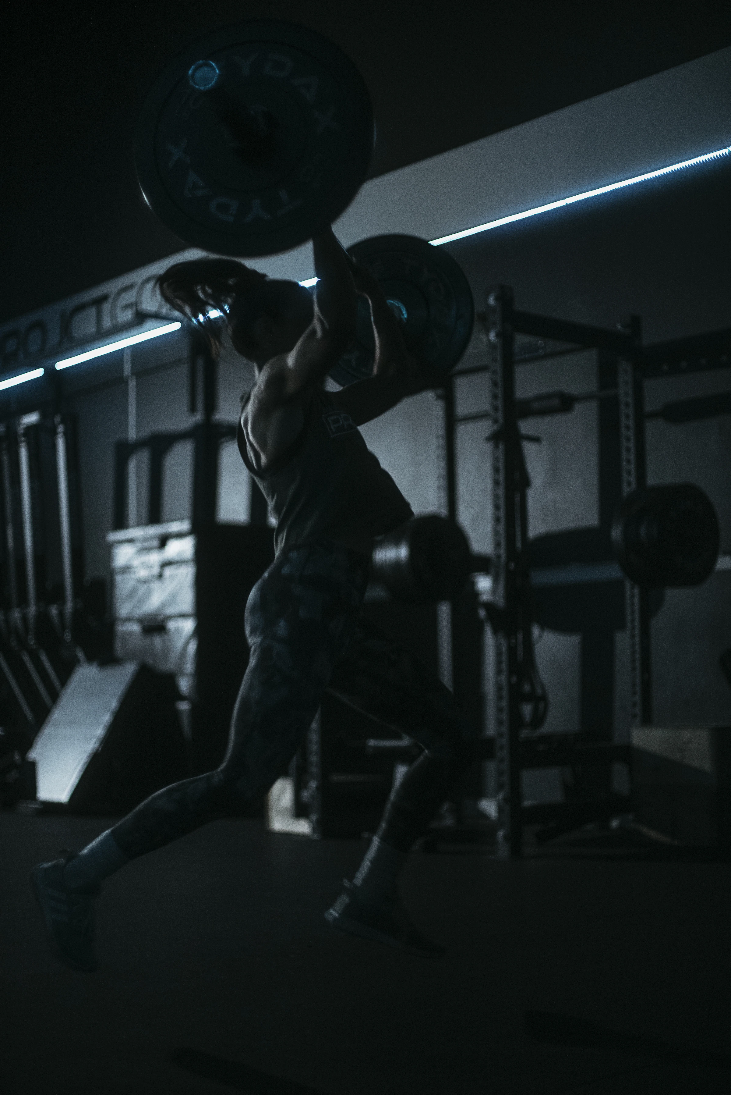 Athlete driving a barbell overhead in a dark training room