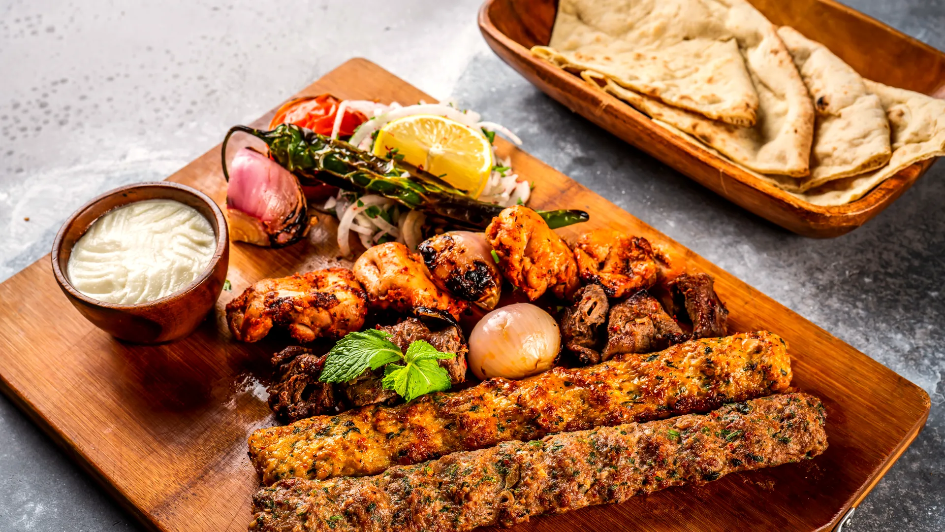 A mixed grill board: seekh kebabs, chicken tikka and lamb over charred onions, naan and raita alongside.