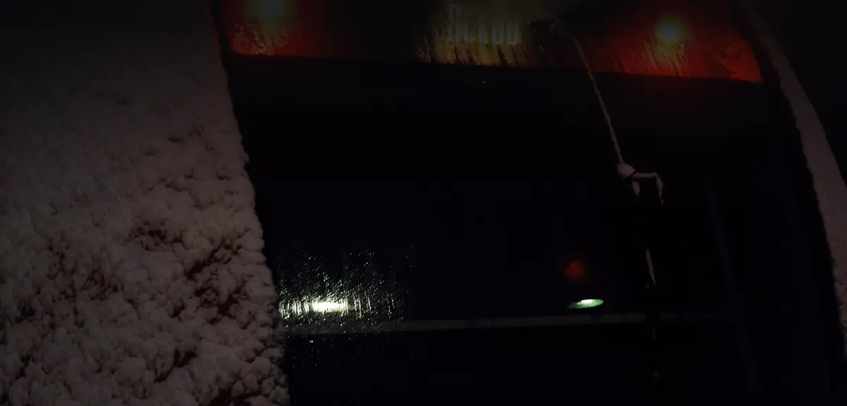 Tail lamps of the last train glowing red through falling snow.