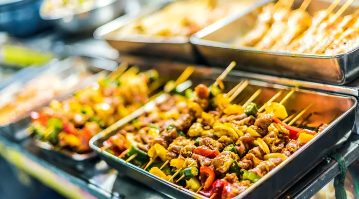 Skewers on a smoking night-market grill, lit by stall lamps.