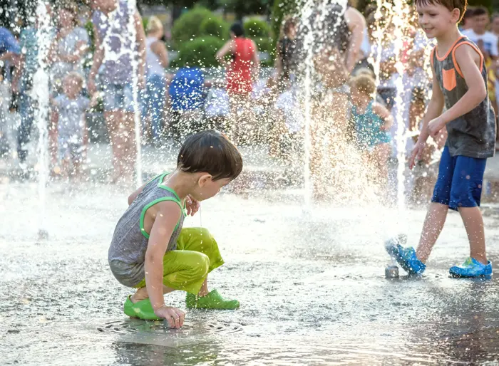A small child crouching happily between fountain jets.