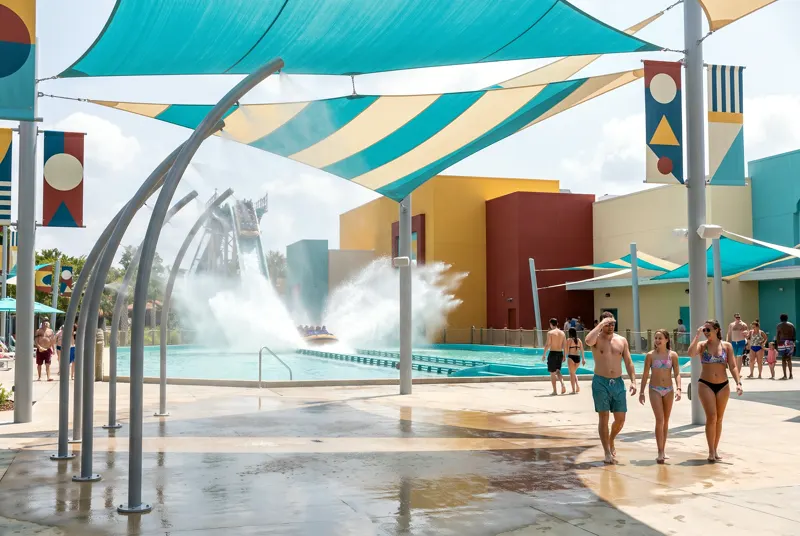Squall's boat hitting the splashdown lagoon under cyan shade sails, mist arcs drifting across the plaza.