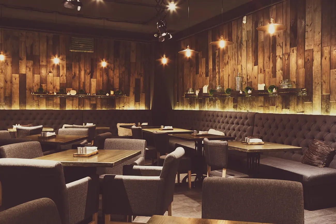 The EMBER dining room — timber tables and low warm light around a central hearth.