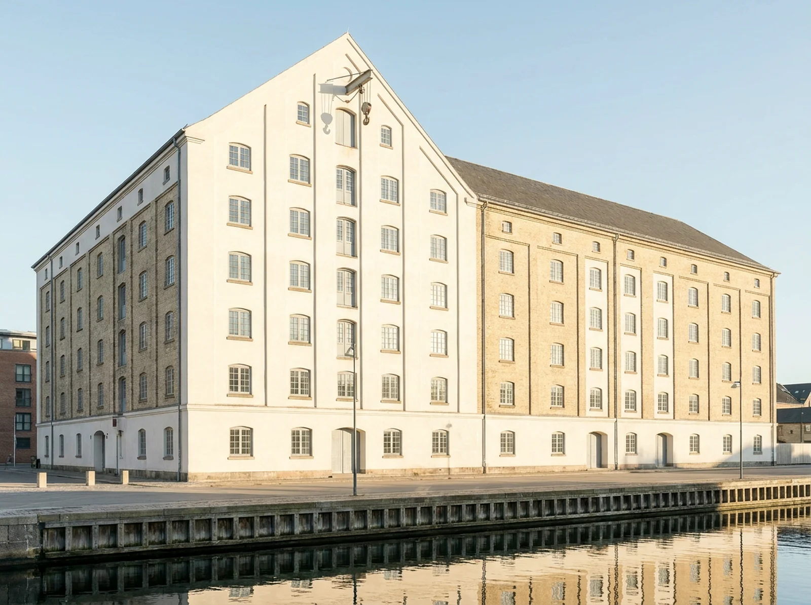 The Grain Store: a tall brick former grain warehouse with rows of small-paned windows, standing at the edge of calm harbour water.