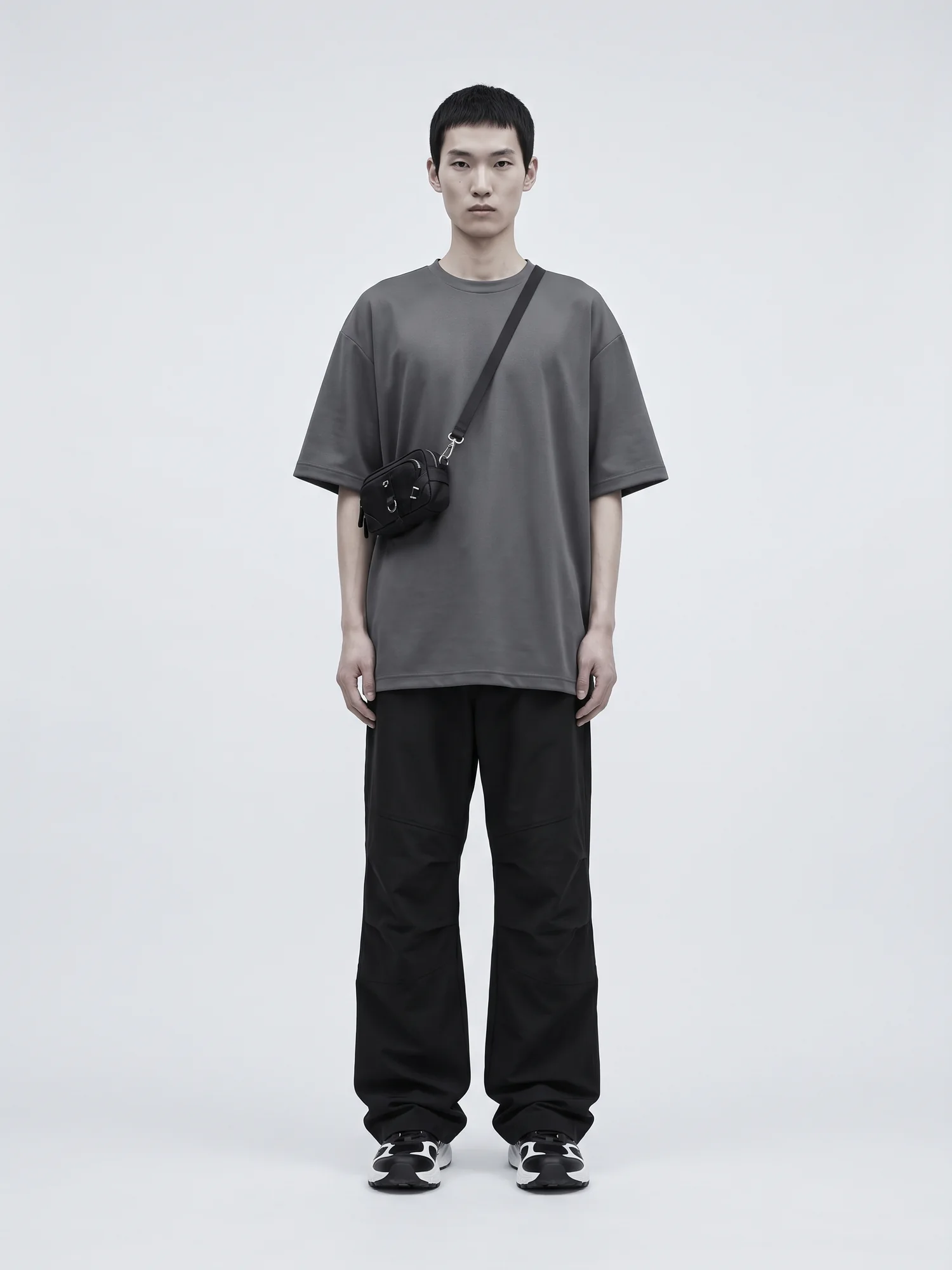 A model in an oversized graphite tee, wide black technical trousers and chunky monochrome sneakers, centered on seamless grey.