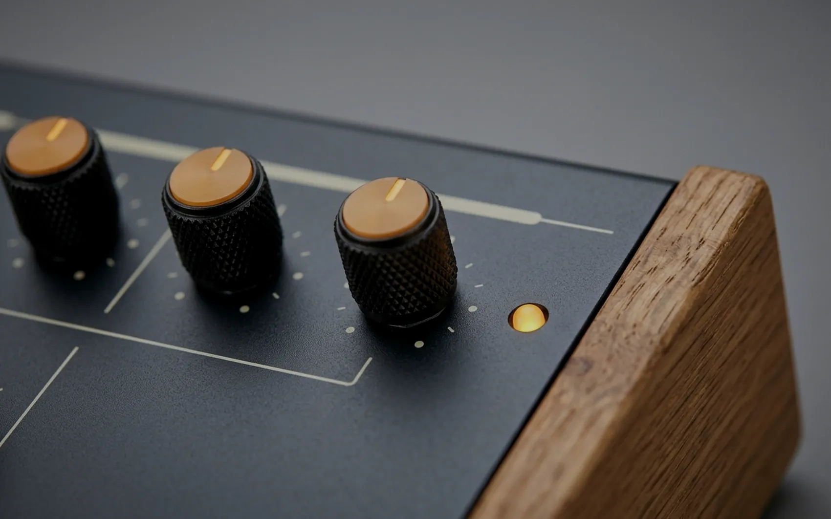 Macro of three knurled knobs with amber caps and a lit amber indicator on a charcoal panel.