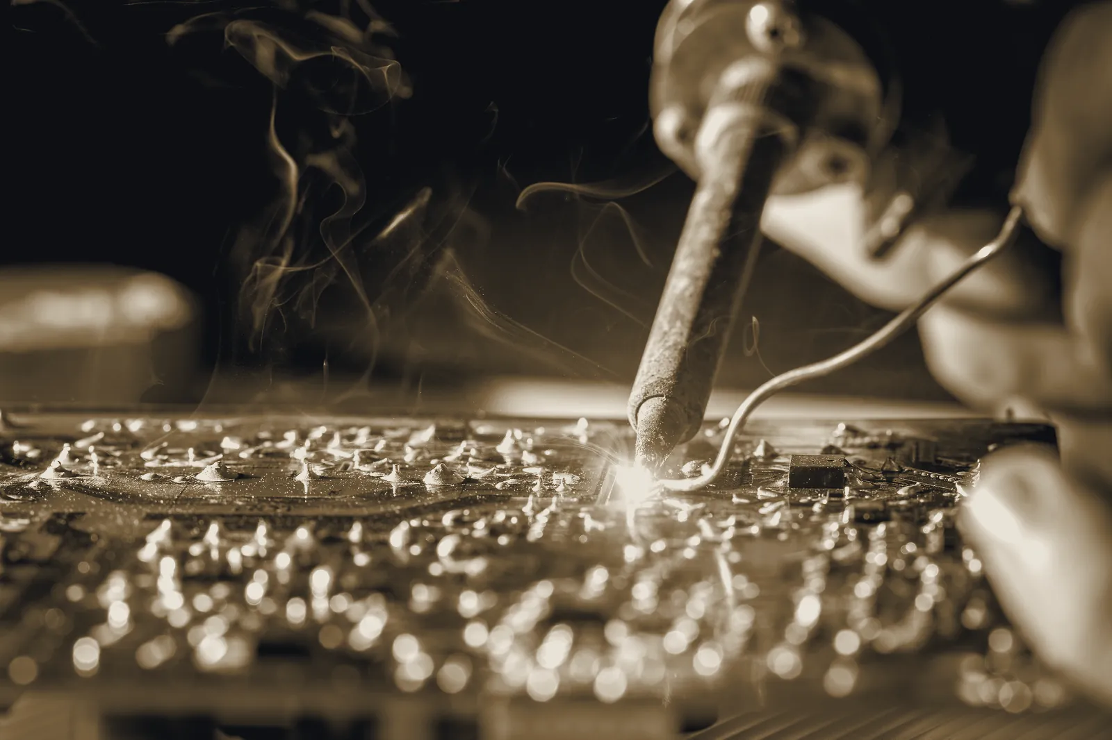 A soldering iron touching a board, solder smoke curling through the light.